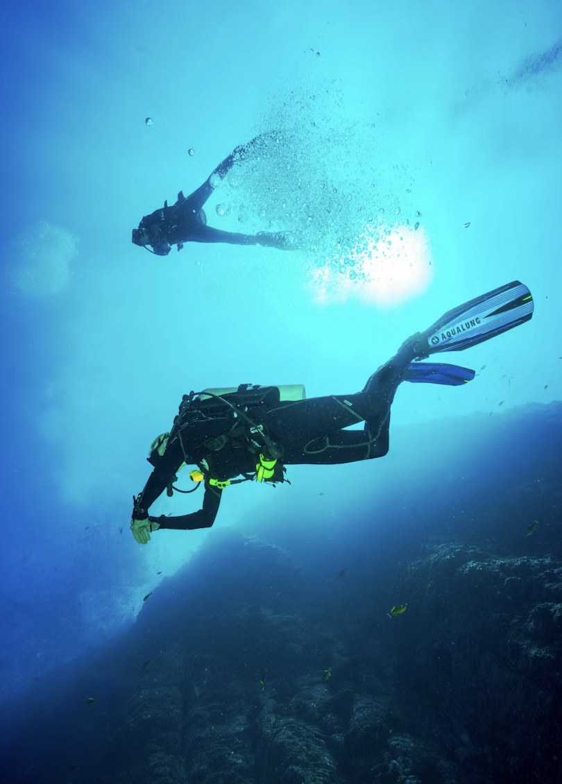 Scuba diver swimming towards sunlight beams in deep tropical waters