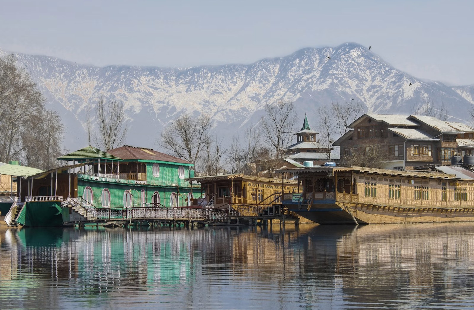 Traditional carved cedarwood houseboats moored against snowy Pir Panjal peaks