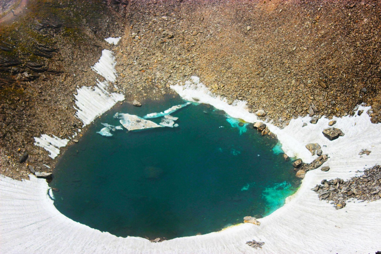 Aerial view of the emerald green mystery lake amidst snow and moraine